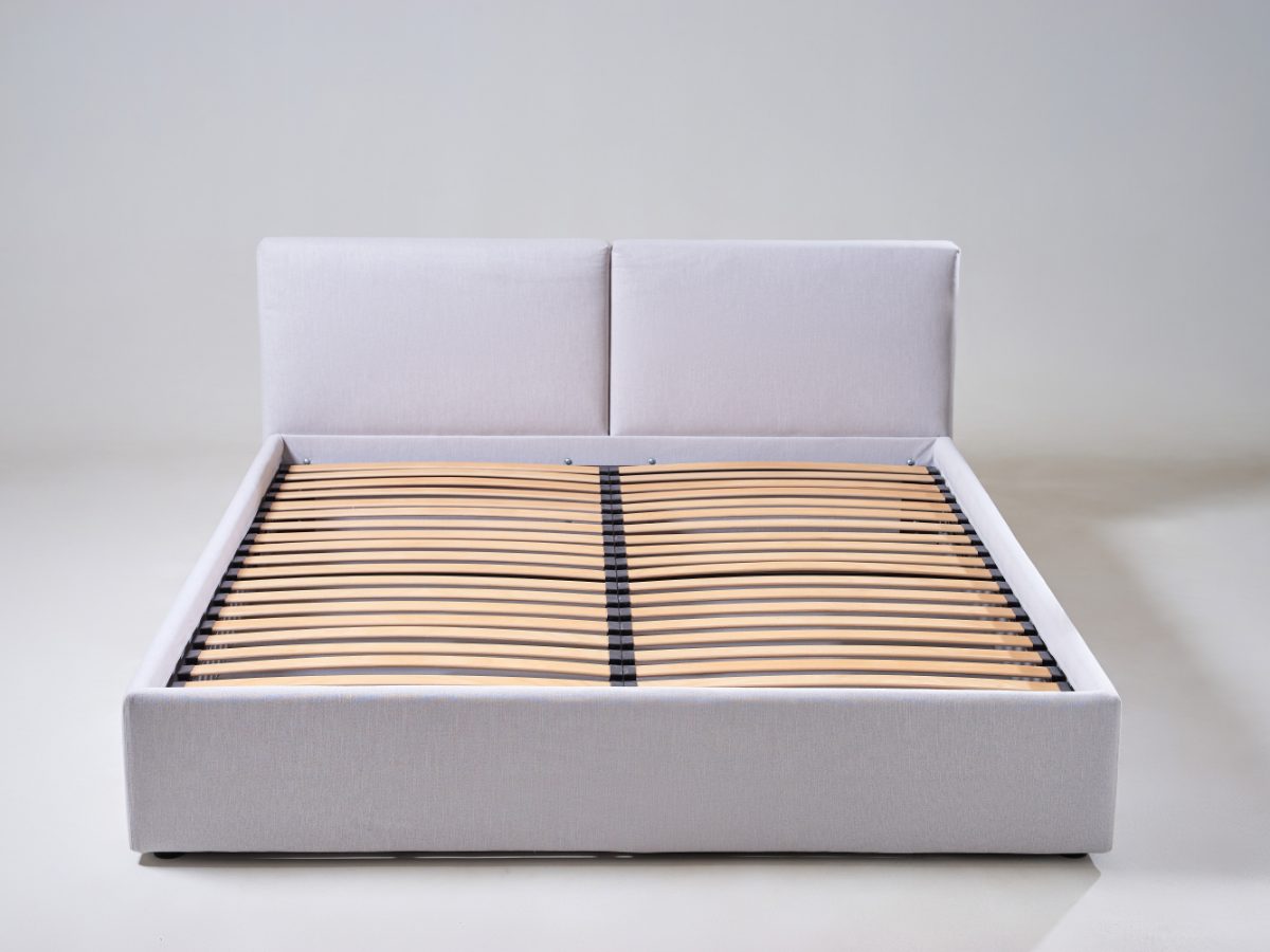 An upholstered bed frame in light grey fabric, with a padded headboard and wooden support slats.